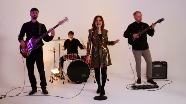 Ett moget musikband med fyra personer i svarta kläder som spelar sång i den ljusa studion - en kvinna i gyllene klänning — Stockvideo