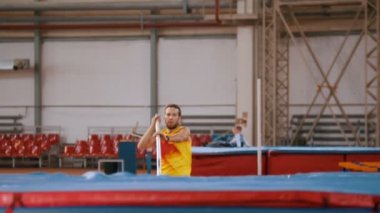 Sırıkla atlama - Sarı tişörtlü uzun boylu sporcu barın üzerinden atlıyor ve koşuyor