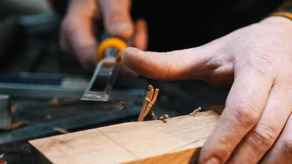 Snickeri i verkstaden - en träarbetare som skär ut rasten på träblocket med mejsel — Stockfoto