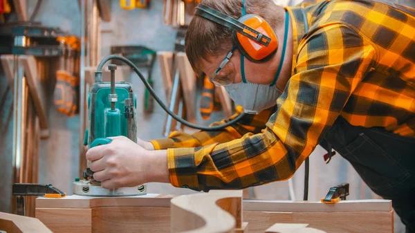 Carpentry indoors - a woodworker polishes the wooden detail with an effort in the workshop