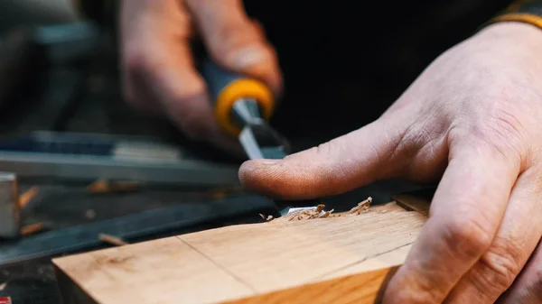 Carpintería interior: un carpintero que corta el hueco del bloque de madera con un cincel — Foto de Stock