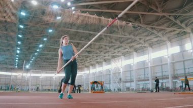 Sırıkla atlama - genç sporcu kadın bir sopayla atlayıp koşmaya hazırlanıyor