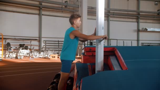 Salto de poste - chico con una camiseta azul está girando la grúa y levantando la barra — Vídeos de Stock