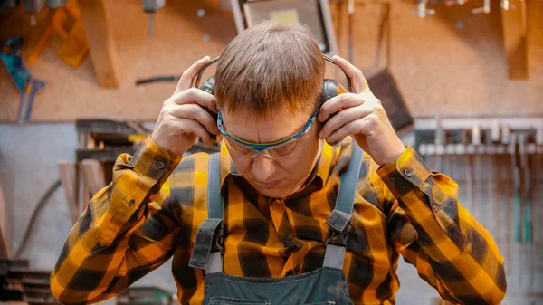 Carpintería en interiores: un carpintero hombre se pone unos auriculares insonorizados protectores —  Fotos de Stock