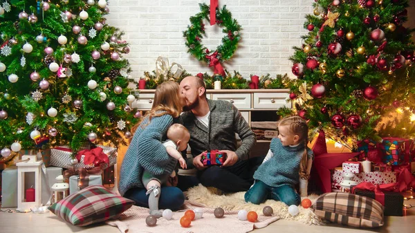 Concepto de Navidad - feliz familia exitosa se sienta en el entorno de Navidad y regalos de intercambio - mamá y papá besándose — Foto de Stock