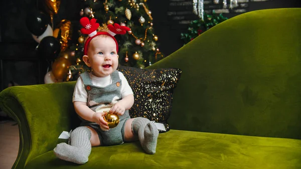Concepto de Navidad - bebé sonriente está sentado en el sofá y jugando con la bola de Navidad — Foto de Stock