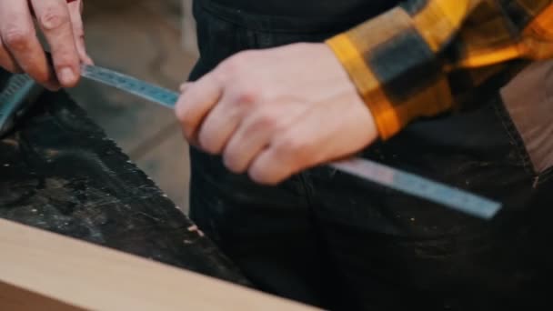 Timmerwerk binnen - een houtbewerker die het houten stuk meet met een meetlat — Stockvideo
