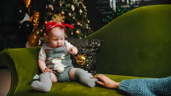 AÑO NUEVO - el bebé está sentado en el sofá y jugando con la bola de Navidad — Foto de Stock