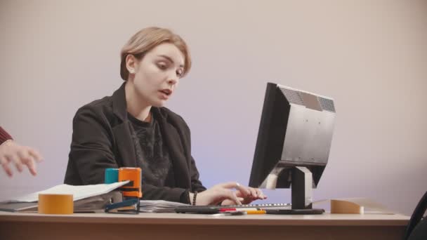 Oficina - una mujer está escribiendo en un ordenador vino un hombre y están hablando — Vídeos de Stock