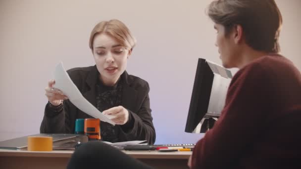 Büro - eine Frau hält Papiere in der Hand und erzählt, was drauf steht und der Mann hört zu — Stockvideo