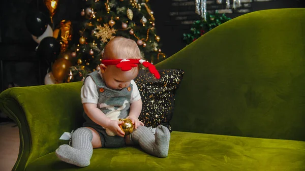 Concepto de Navidad - el bebé está sentado en el sofá y jugando con la bola de Navidad — Foto de Stock
