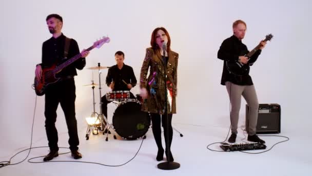 Una banda musical de cuatro personas vestidas de negro tocando la canción en el estudio brillante - una mujer con un vestido de oro — Vídeos de Stock