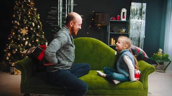 Concepto de Navidad - un padre con una hija intercambiando regalos en Navidad - papá escondiendo un regalo a sus espaldas — Foto de Stock