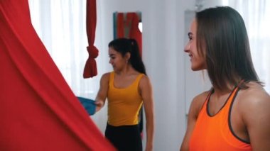 Hava yogası - Atletik bir kadın ve antrenörü yoga için kırmızı bir hamağın örtüsünü yayıyorlar