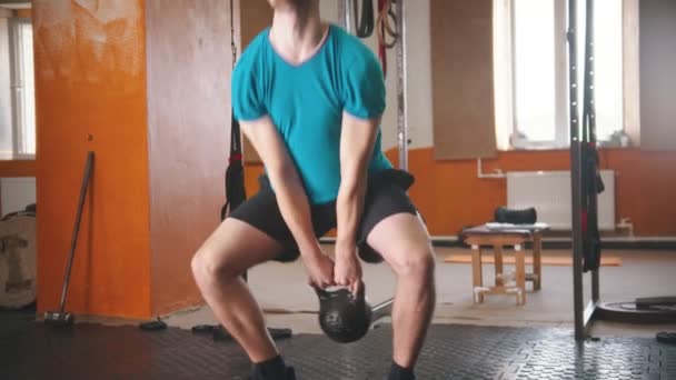 Een man in een blauw t-shirt krakend met een gewicht in zijn handen — Stockvideo