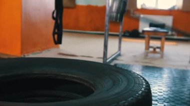 Spor eğitimi. Spor salonunda dövmeli bir sporcu büyük bir araba lastiğine çekiçle vuruyor.