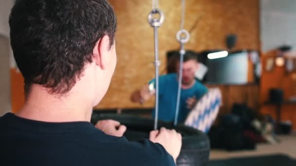 Treinamento de cavaleiros - um homem treinando suas habilidades de espada no bando de pneus - outro homem segurando o pacote — Vídeo de Stock