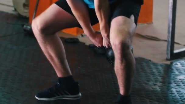 Sportliches Training - ein Mann im blauen T-Shirt hockt mit einem Gewicht in den Händen — Stockvideo