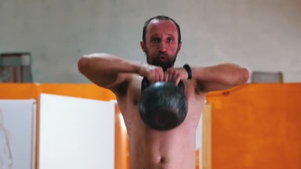 Entraînement sportif - un homme torse nu accroupi avec un poids dans les mains — Video