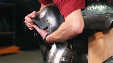 Şövalyeler antrenman yapıyor. Bir adam bacaklarına metal koruyucu zırh takıyor.