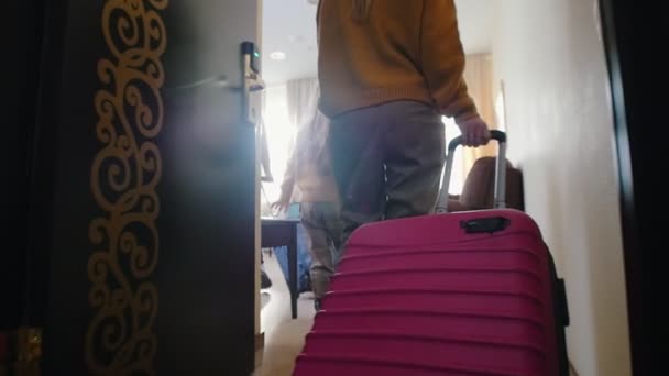 En familj som kommer in i ett hotellrum - drar sitt färgglada bagage efter dem — Stockvideo