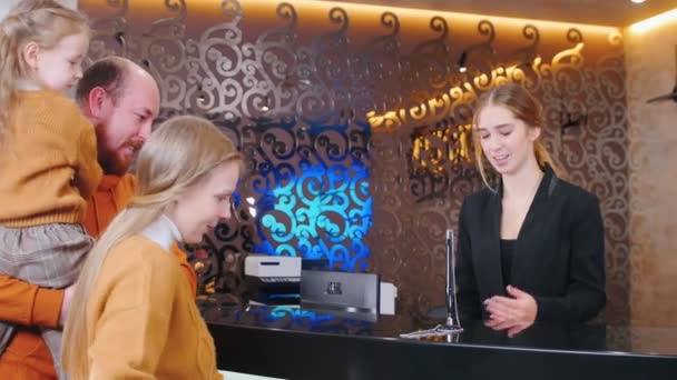 Un check-in familial à l'hôtel - une femme à la réception saluant la famille — Video