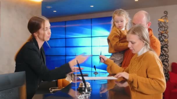 Een familiecontrole in het hotel - een vrouw die de papieren voor kamerhuur zingt bij de receptie — Stockvideo