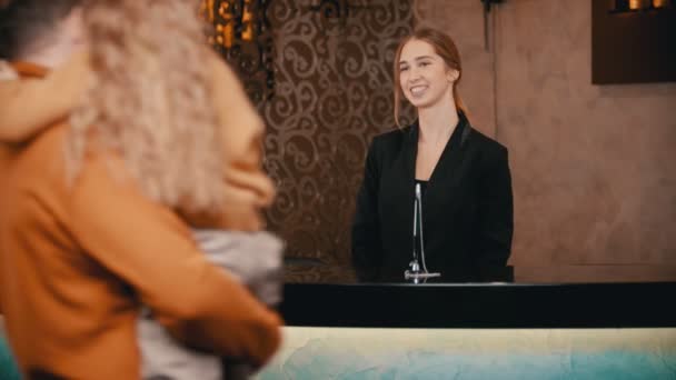 Una familia registrándose en el hotel de lujo - una mujer sonriente saludando a la familia en la recepción y dando un folleto al huésped — Vídeos de Stock