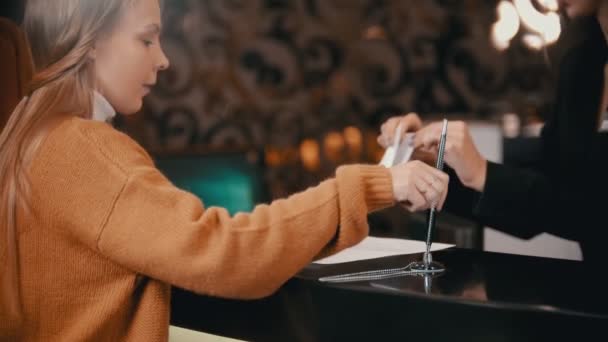 Registrarse en el hotel de lujo: una mujer firma los papeles y toma el folleto de una mujer en la recepción — Vídeos de Stock