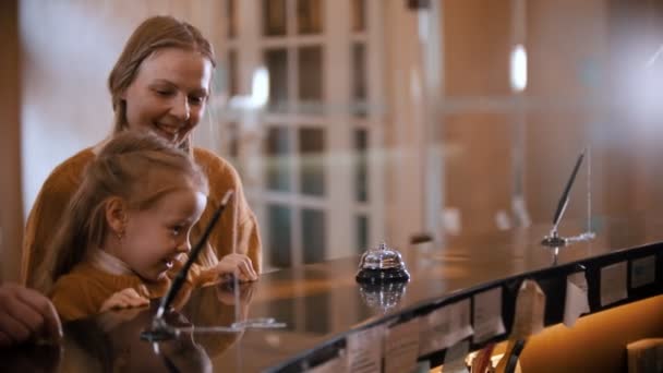 Una famiglia che fa il check-in nell'hotel di lusso - una bambina sale sullo stand della reception — Video Stock