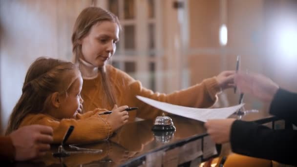 Une famille vérifie à l'hôtel de luxe - une petite fille joue avec un crayon avant que sa mère ne lui prenne pour signer les papiers — Video