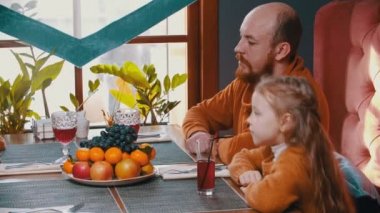 Otel restoranında oturup üzüm yiyen bir aile.