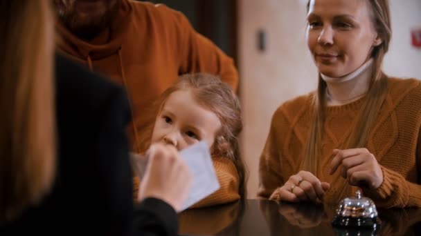 Una famiglia che fa il check-in in hotel - una donna alla reception spiega alla famiglia i suoi privilegi in hotel e dà loro un opuscolo e le chiavi — Video Stock