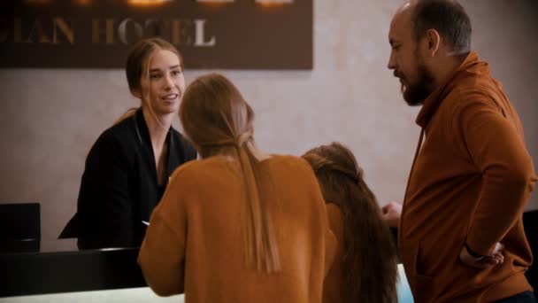 En familjekontroll på lyxhotellet - en kvinna i receptionen förklarar för familjen sina privilegier på hotellet som har en broschyr — Stockvideo