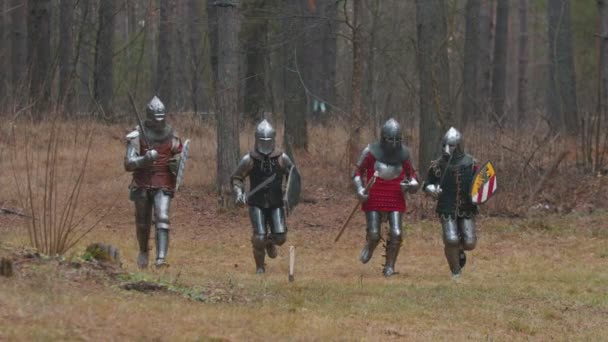 Τέσσερις άνδρες ιππότες τρέχουν στη σειρά στο δάσος με πλήρη θωράκιση κρατώντας όπλα — Αρχείο Βίντεο