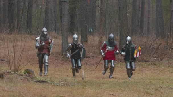 Vier mannen ridders rennen in de rij in het bos in volle wapenrusting. — Stockvideo