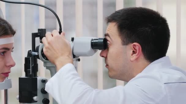 Офтальмологическое лечение - молодая красивая женщина проверяет остроту зрения специальным оборудованием в просторном кабинете врача — стоковое видео
