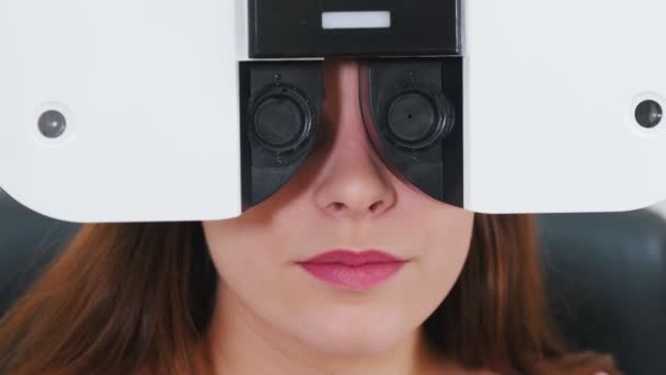 Trattamento oftalmologico - una giovane donna che controlla la sua acutezza visiva con una speciale apparecchiatura optometrica - una macchina che cambia lenti — Video Stock