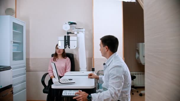 Zabieg okulistyczny - młoda uśmiechnięta kobieta sprawdzająca ostrość wzroku na sprzęcie okulistycznym u lekarza — Wideo stockowe