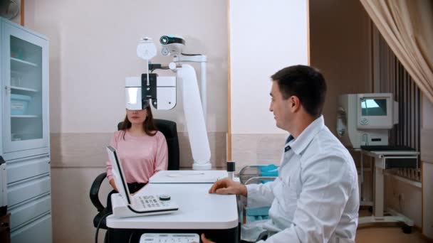 Tratamiento oftalmológico - mujer joven comprobando su agudeza visual en un equipo optométrico - guardando el equipo y continuando la consulta — Vídeos de Stock