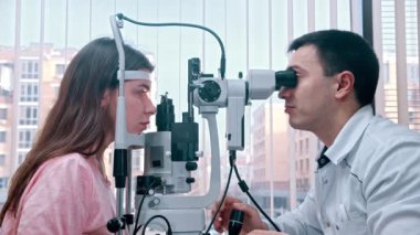Oftalmoloji tedavisi - genç kadınların görsel keskinliklerini ışığı kullanarak kontrol eden bir doktor - panoramik pencerenin arka planında geniş bir dolap