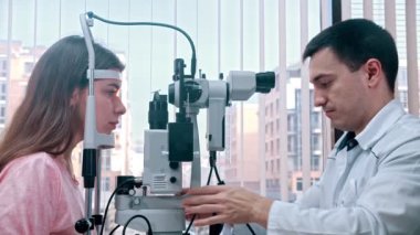 Oftalmoloji tedavisi - genç kadınların görme keskinliğini ışık kullanan özel bir aletle kontrol eden bir doktor - panoramik pencereli geniş bir dolap