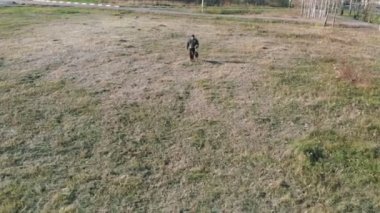 Alman çoban köpeğiyle tarlada yürüyen bir köpek bakıcısı.