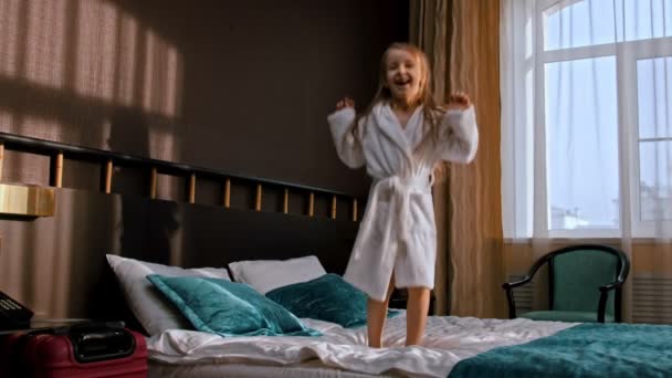 Mała dziewczynka z długimi włosami skacząca na łóżku w pokoju hotelowym — Wideo stockowe
