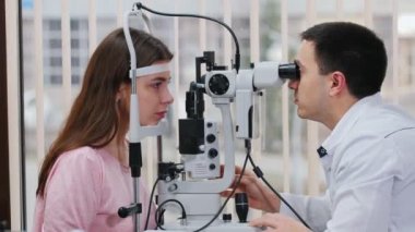 Oftalmoloji tedavisi - özel bir makine ile genç kadınların görme keskinliğini kontrol eden bir doktor - panoramik pencereli geniş bir dolap