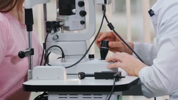 Tratamiento oftalmológico: un médico que comprueba la agudeza visual de las mujeres jóvenes con una máquina especial en un gabinete espacioso — Vídeos de Stock