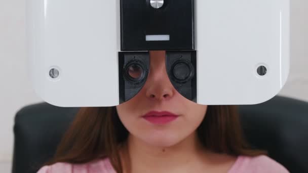 Tratamento oftalmológico - uma jovem mulher com lábios rosa brilhantes verificando sua acuidade visual com um equipamento especial de optometria - conversando enquanto seus olhos estão fechados com uma máquina — Vídeo de Stock