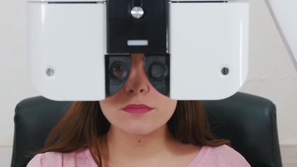 Офтальмологічне лікування - молода жінка з яскраво-рожевими губами, що перевіряє гостроту зору за допомогою спеціального обладнання для оптометрії — стокове відео