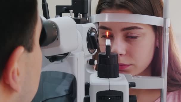 Zabieg okulistyczny - młoda kobieta z różowymi ustami sprawdzająca ostrość wzroku - reakcja źrenicy na światło — Wideo stockowe