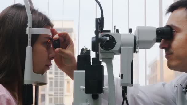 Augenheilkunde - Eine junge Frau überprüft ihre Sehschärfe mit einem Gerät - Pupillenreaktion auf Licht wirft die Linse - heller Schrank — Stockvideo